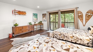 A modern bedroom with a large bed, a wooden dresser, a desk, and a view of the outdoors. - Modern Primrose (Big Bear Lake)
