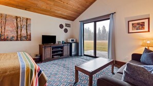 A room with a wooden ceiling, a television on a wooden cabinet, a sofa, a table, and a view through a glass door.