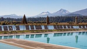 A swimming pool with lounge chairs and umbrellas, surrounded by a forest and mountains in the background.