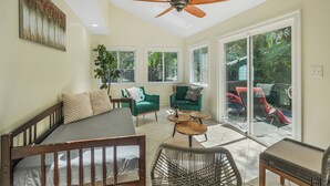 Une pièce spacieuse comprenant un lit, un fauteuil vert, une table basse en bois et un ventilateur de plafond.