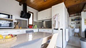 A modern kitchen with white cabinets, a microwave, a stove, and a dining area with a table and chairs. - Chalet Cottage 50 m from Lake with View, Private Terrace, and Wi-Fi (Le Vernet-Chaméane)