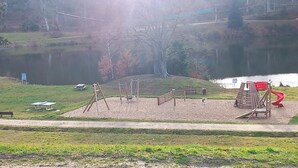 A playground with swings, a slide, and a sandbox near a lake. - Chalet Cottage 50 m from Lake with View, Private Terrace, and Wi-Fi (Le Vernet-Chaméane)