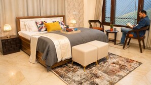 Une chambre à coucher comprenant un lit, des tables de chevet, un fauteuil de lecture, une fenêtre avec vue et une petite table sur laquelle est posée une plante.
