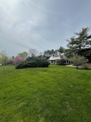 A large, open grassy area with a house featuring a stone chimney and a porch.