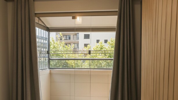 A bedroom with a bed, curtains, a hanging light fixture, and a view of a balcony with buildings. - 450m from the beach. Functional apartment, 500MB Wi-Fi, garage, sleeps up to 5 people. (Balneário Camboriú)