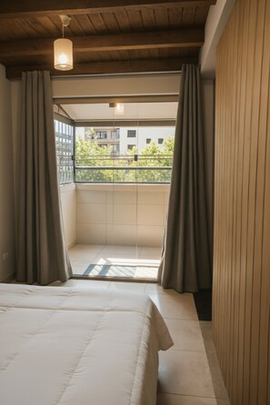 Un dormitorio con cama, cortinas, lámpara colgante y vista a un balcón con edificios.