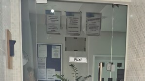 A reception area with a glass door, a 'PUXE' sign, a bulletin board, and a potted plant. - 450m from the beach. Functional apartment, 500MB Wi-Fi, garage, sleeps up to 5 people. (Balneário Camboriú)