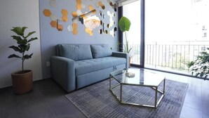 En moderne stue med en grå sofa, et glasbord, et mønstret tæppe, en potteplante og en væg med hexagonmønstre.