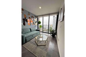 A modern living room with a green sofa, a glass coffee table, and a city view through large windows. - Cozy home office, loft in Guadalajara (Guadalajara)