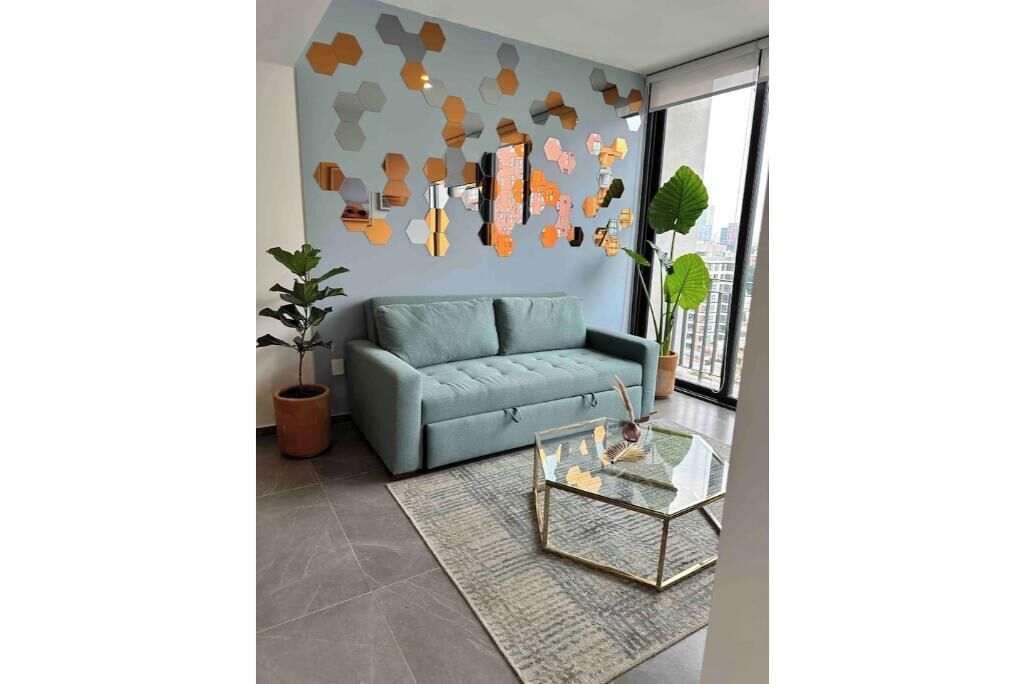 A modern living room with a grey sofa, a glass coffee table, and a geometric wall decoration.