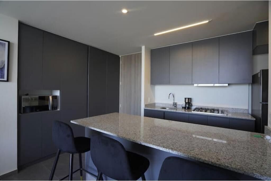 A modern kitchen with dark cabinetry, a granite countertop, and a bar area with two stools.