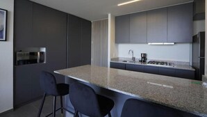 A modern kitchen with dark cabinetry, a granite countertop, and a bar area with two stools. - Splendid apartment in the heart of Colonia Americana (Guadalajara)