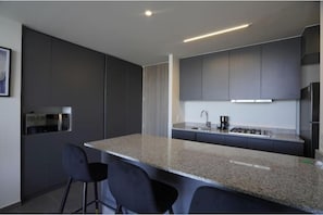 A modern kitchen with dark cabinetry, a granite countertop, and a bar area with two stools. - Splendid apartment in the heart of Colonia Americana (Guadalajara)