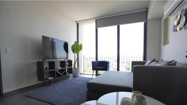 A modern living room with a flat-screen TV, a sofa, a coffee table, and a large window with a view. - Splendid apartment in the heart of Colonia Americana (Guadalajara)