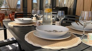 Une table à manger dressée avec des assiettes, des bols, des verres et une bouteille d’eau.