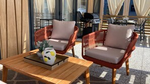 Un espace extérieur aménagé avec des chaises en osier, une table en bois et un barbecue.