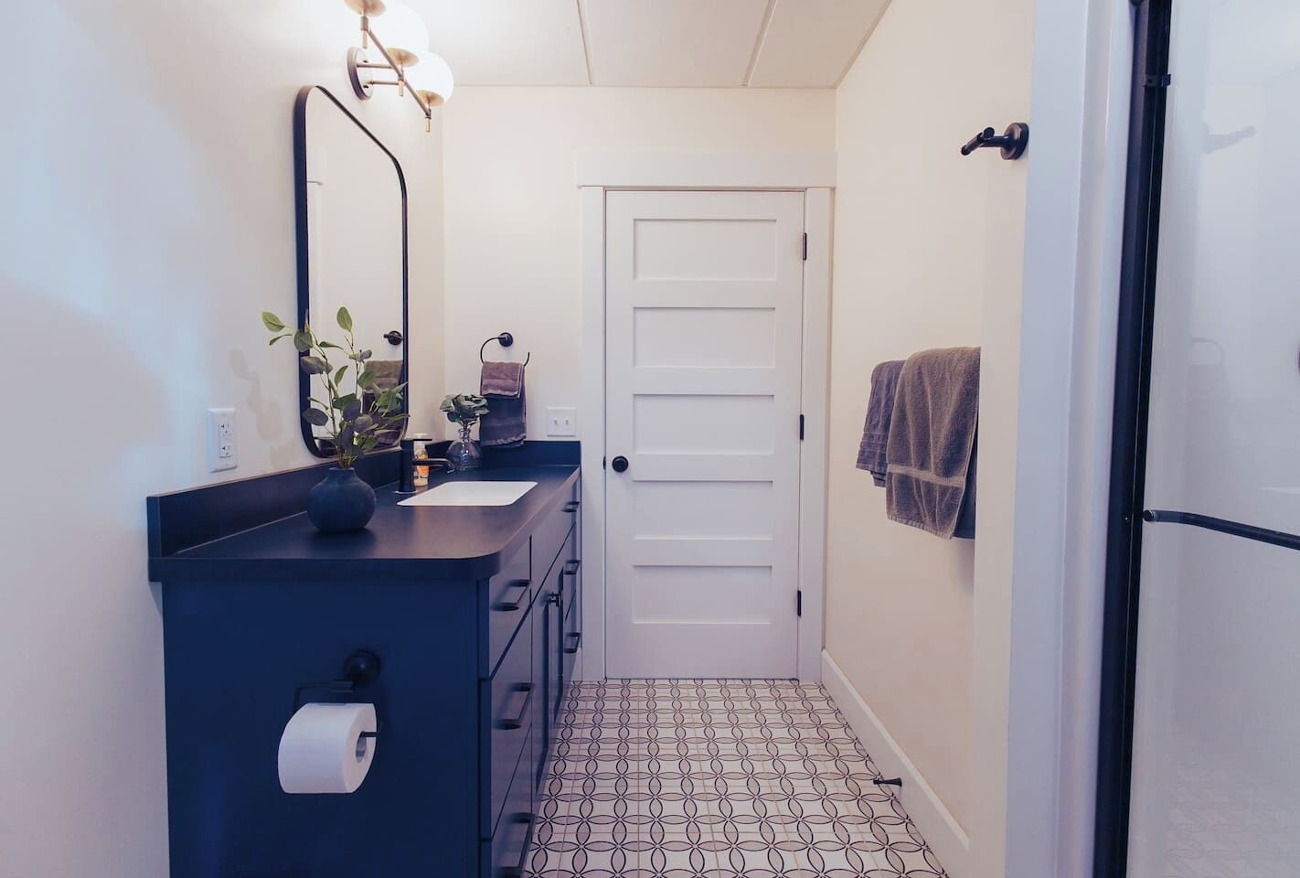 A bathroom with a dark blue vanity, a white door, a towel hanging on the wall, and a patterned floor.