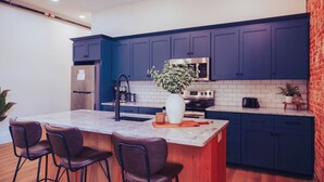 Een moderne keuken met donkerblauwe kastjes, een centraal eiland met barkrukken, een roestvrijstalen koelkast en een magnetron.