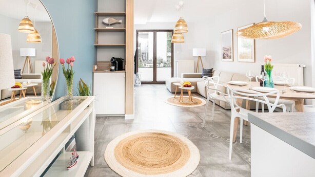 Une cuisine moderne avec des meubles blancs, un grand miroir et un coin repas comprenant une table ronde et des chaises.