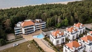 Un hôtel à plusieurs étages doté d’une piscine, entouré d’une forêt dense et situé près d’une plage.