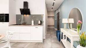 Une cuisine moderne équipée d’une cuisinière intégrée, d’un évier et d’un plan de travail. Un couloir mène à une salle de bain avec un miroir et des toilettes.