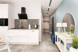 Una cocina moderna con estufa integrada, un lavamanos y una encimera. Hay un pasillo que conduce a un baño con espejo y retrete.