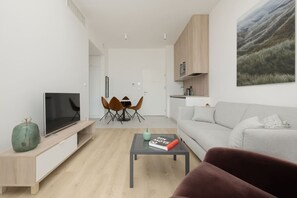 Un salon moderne doté d’un téléviseur à écran plat, d’un coin repas avec des chaises, d’un canapé gris et d’une table basse.