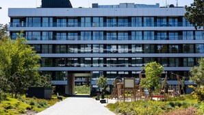 A modern multi-story building with a central entrance, surrounded by greenery and a playground. - Widok na Morze | Przy Plaży | Taras | Shellter (Rogowo)