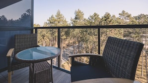 Ein Balkon mit Korbmöbeln und einem Glastisch, mit Blick auf ein bewaldetes Gebiet.
