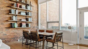 Un espace repas avec un mur en briques, des étagères et une vue sur la ville grâce à de grandes fenêtres.