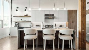 Une cuisine moderne dotée d’un îlot central, de trois chaises, de luminaires suspendus et d’une grande fenêtre.