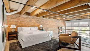 Une chambre avec un mur en briques, un grand lit, une chaise et une fenêtre.