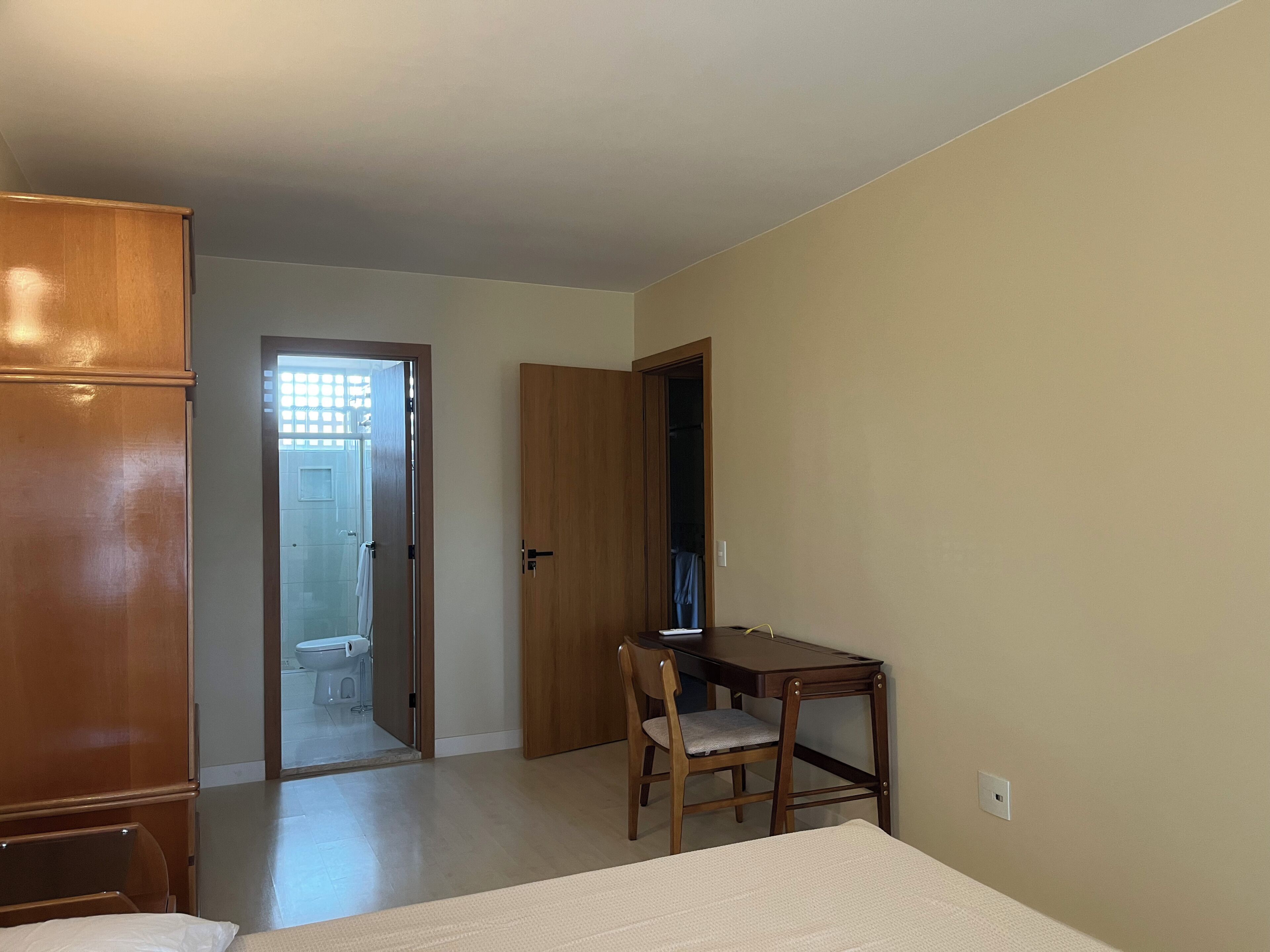 Un dormitorio con una cama, un armario de madera, un escritorio con una silla y una puerta que da a un baño.