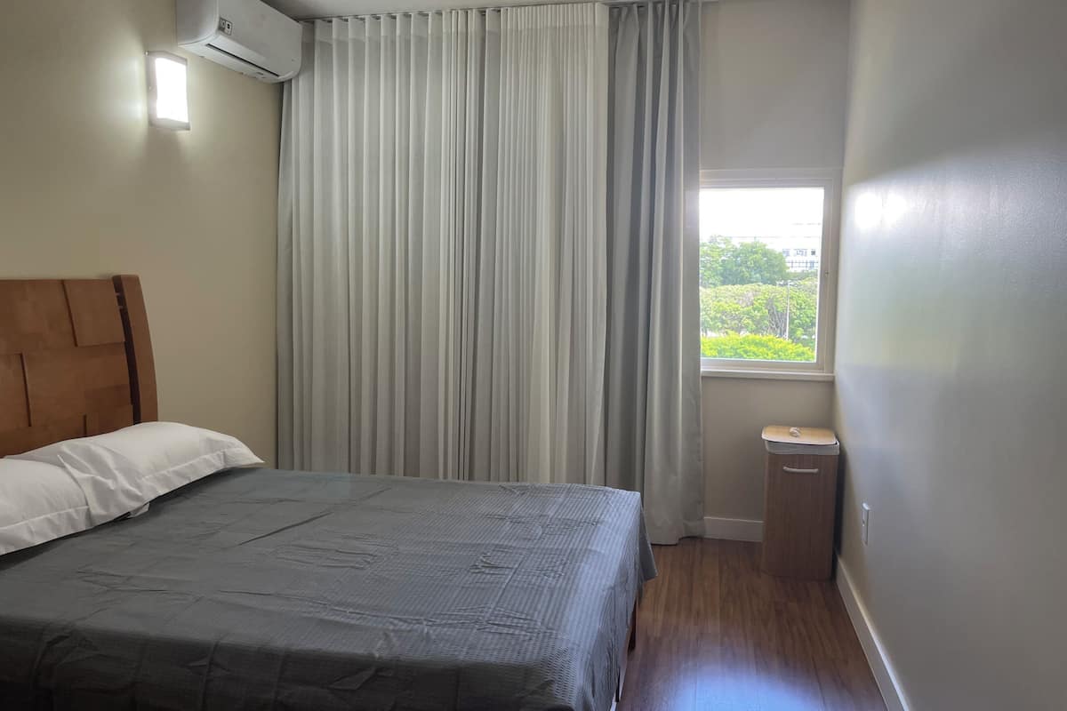 A bedroom with a bed, a window, a nightstand, and an air conditioning unit.