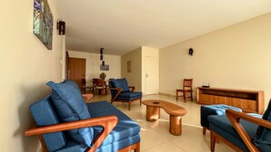 A living room with a sofa, chairs, a coffee table, and a dining area with a table and chairs. -  Quartos Premium na 206 Sul  Banheiro Privativo (Brasília)