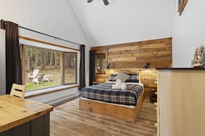 A bedroom with a bed, a desk, and a view of the outdoors.