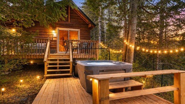 Una cabaña de madera con jacuzzi, terraza de madera y escalera que lleva a la entrada.