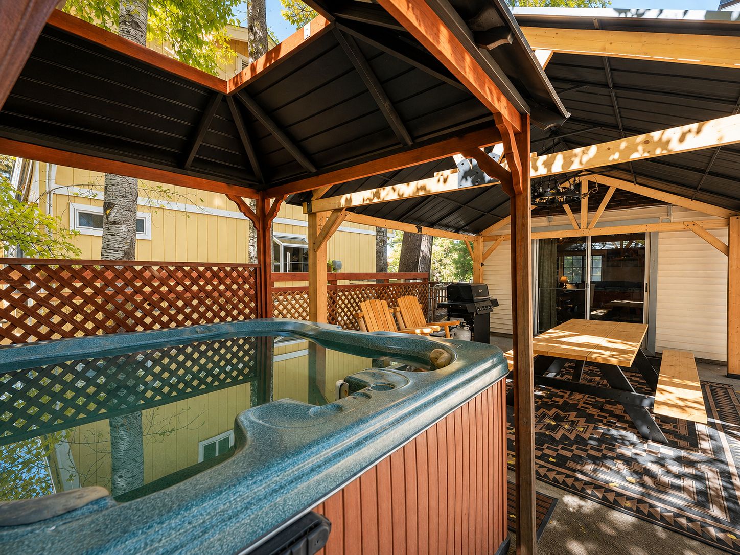 Zona de hidromasaje al aire libre con una terraza de madera, un área de estar cubierta y vista a un edificio residencial en el fondo.