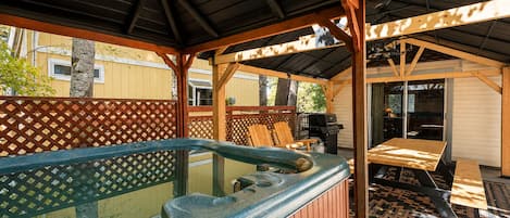 Een buitenzwembad met houten terras, een overdekte zithoek en uitzicht op een woongebouw op de achtergrond.