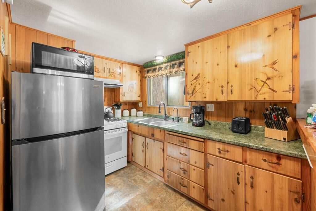 A kitchen with wooden cabinets, stainless steel appliances, a granite countertop, and a window with a decorative valance.
