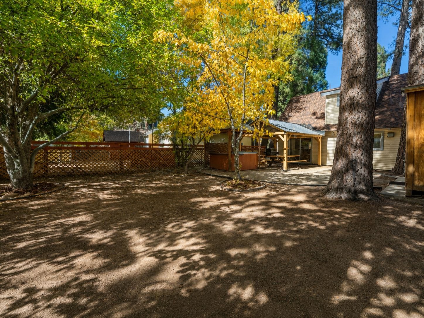 A backyard with a covered patio, a barbecue grill, and a wooden fence.