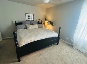 Une chambre à coucher avec un lit, une lampe de chevet, un tableau encadré au mur et une plante.