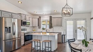 A modern kitchen with stainless steel appliances, a central island with stools, and a hanging light fixture. - Montana Retreat (Billings)