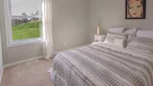 A bedroom with a large window, a bed with patterned bedding, a bedside table with a lamp, and a framed picture on the wall. - Montana Retreat (Billings)