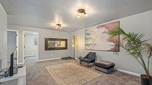 A spacious living room with a large painting, a potted plant, a chair, a bench, and a desk with a computer. - Montana Retreat (Billings)