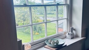 A window with a view of a green landscape, a decorative plate, and a small figurine on a shelf. - Farnah House Barn (Belper)