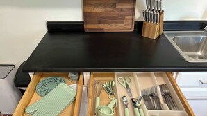 Un piano di lavoro in cucina con tagliere, blocco coltelli e vari utensili nei cassetti.