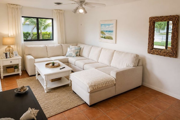 A living room with a white sectional sofa, a white coffee table, a small side table, a lamp, and a framed picture on the wall.