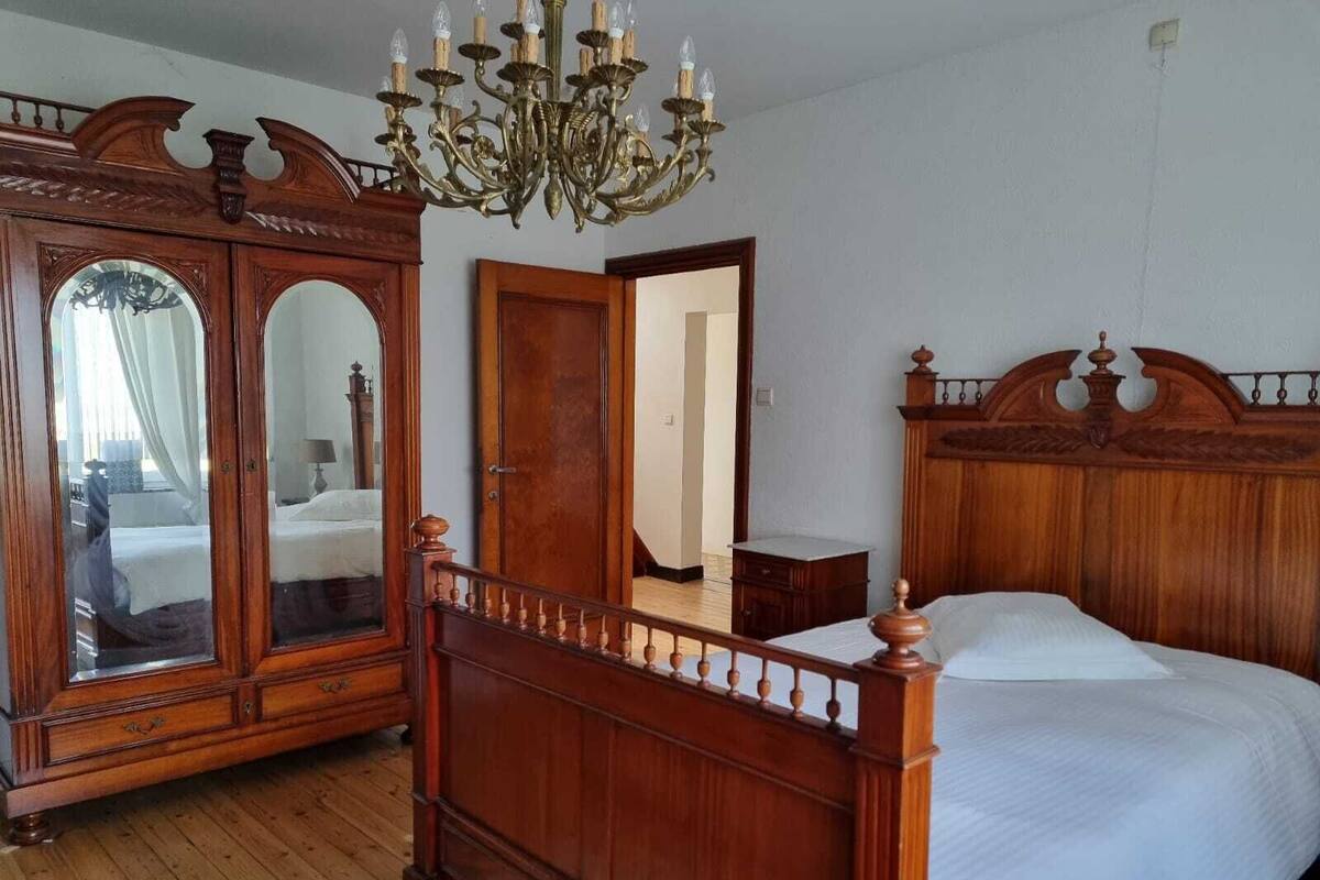 A bedroom with a wooden bed, a large mirror, a wardrobe, and a chandelier.