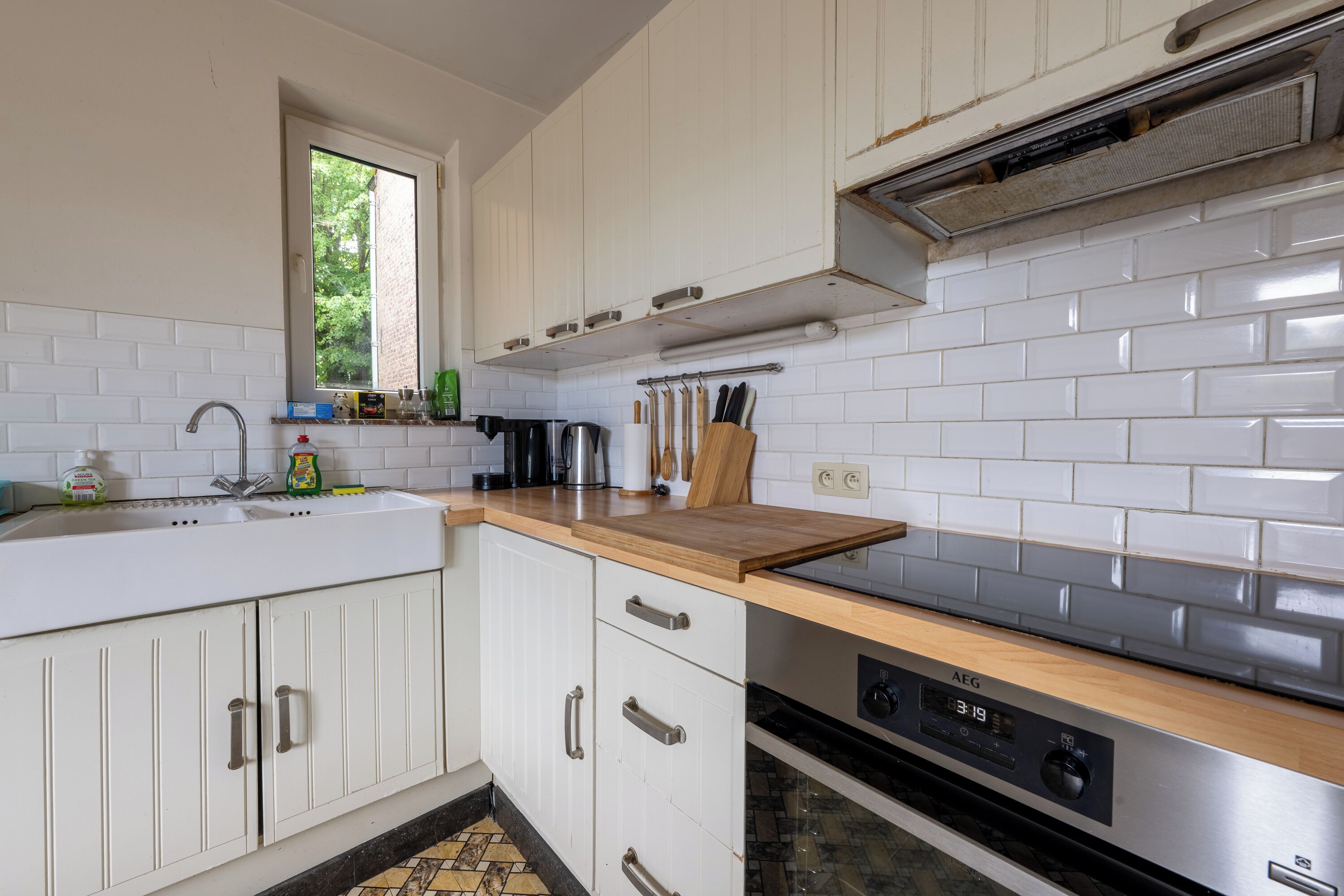 A kitchen with white cabinets, a wooden countertop, a stainless steel range hood, and a window with a view of greenery.